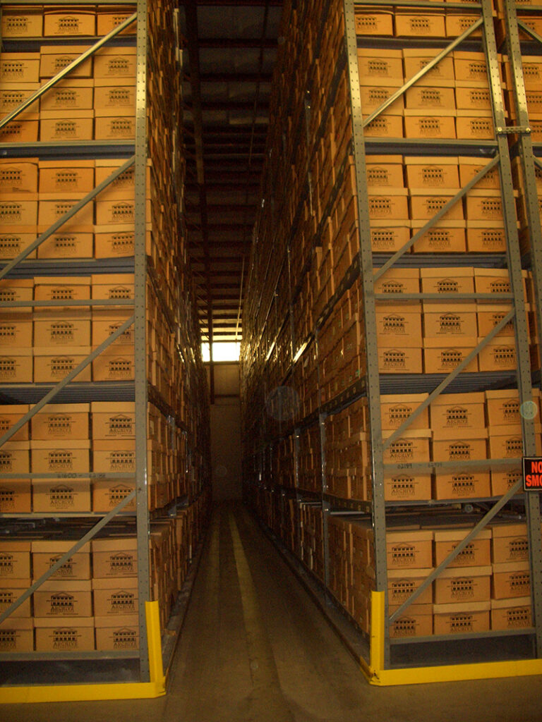 inside of archive storage facility with an tall stack of document storage boxes organized and filed on shelves.